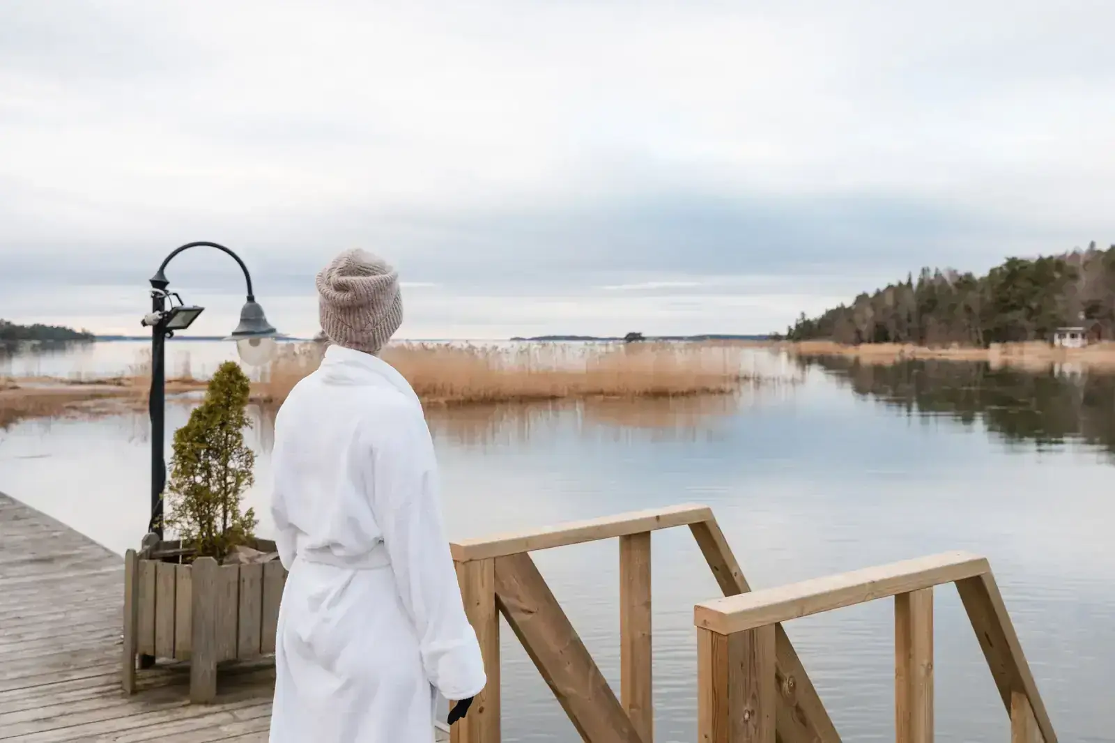 Valkoiseen kylpytakkiin pukeutunut henkilö katsoo talviselle merelle laiturilta